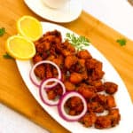 Plate of chicken fritters with lemon and onion rings with chai or tea in the background