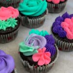 Chocolate cupcakes with teal, pink and purple flowered frosting.