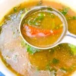 A close up of rasam in a ladle with red chili.