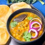 chole in a black bowl garnished with onions and cilantro and served with puri.