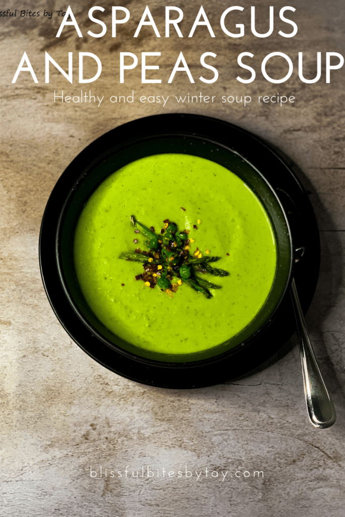 Peas and asparagus soup in a black bowl with roasted asparagus, peas and chilli flakes on top.