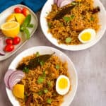 Chicken Biryani in two bowls with onion slices, halved eggs on top.