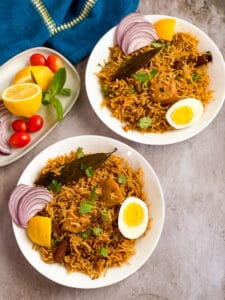 Chicken Biryani in two bowls with onion slices, halved eggs on top.