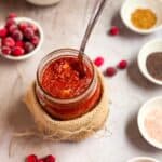 Cranberry pickle in a mason jar with spices in the background.