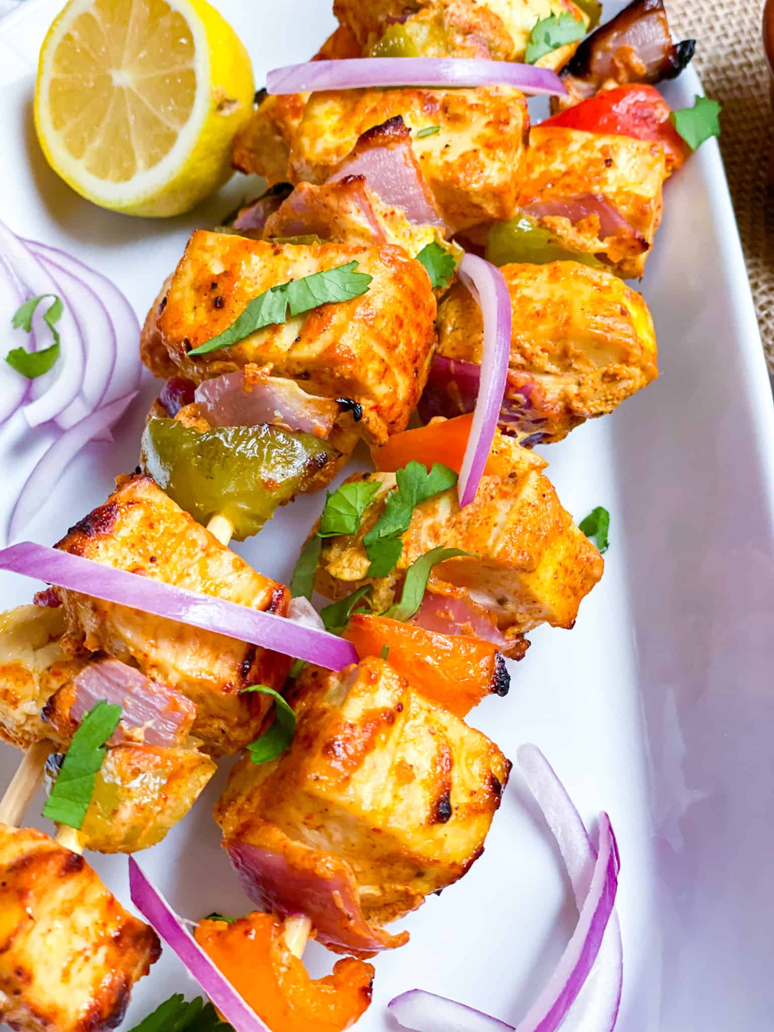 Tofu tikka on skewers garnished with onion slivers and lemon wedges.