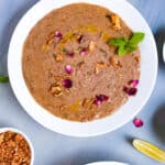 A bowl of Hyderabad mutton Haleem with rose petals, ghee, fried onions and mint on top.