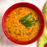 Radish greens dal in a red bowl with curry leaves on top.