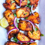 Andhra style fish fry in a white rectangular plate with onions and cilantro garnish.