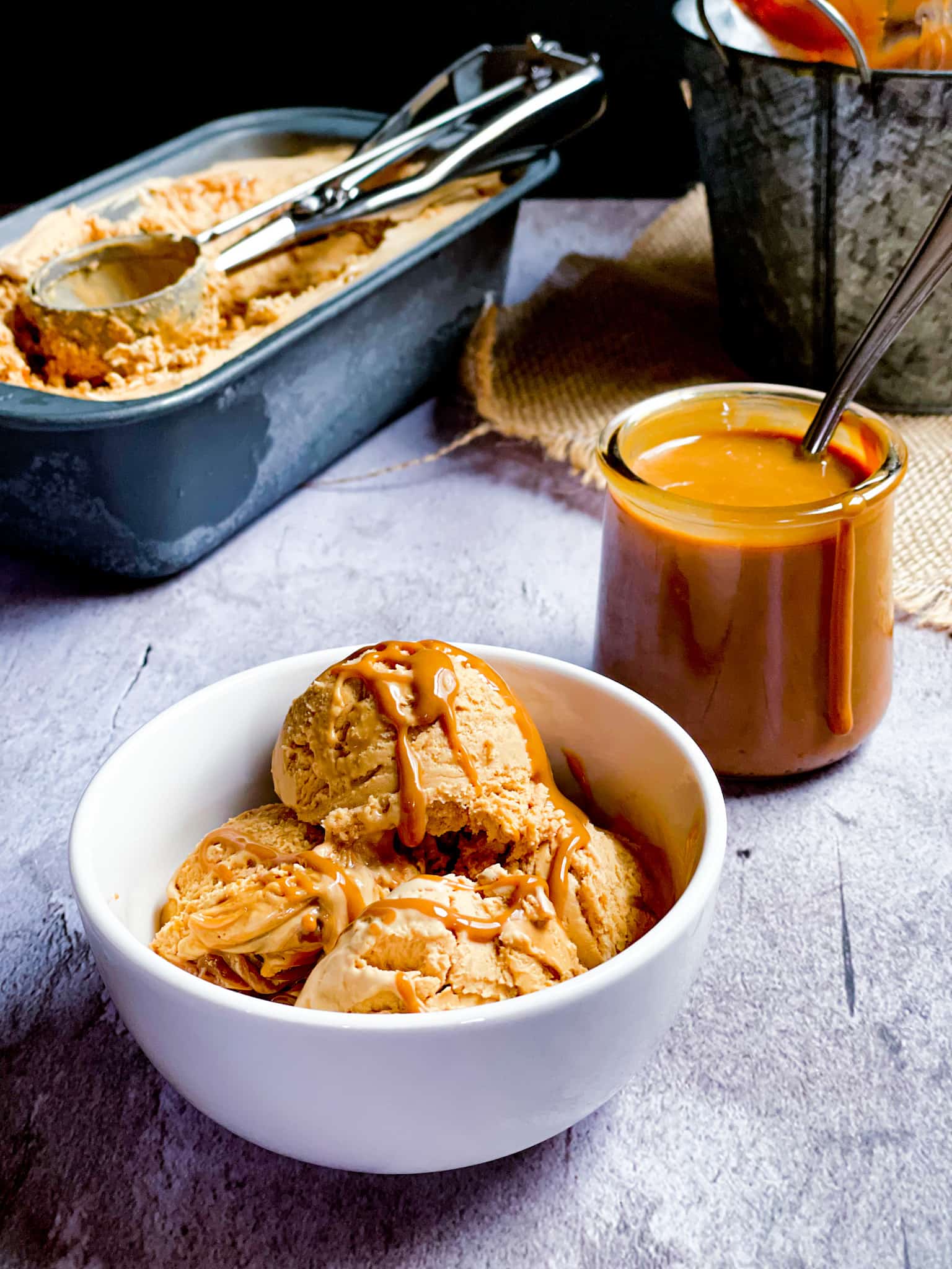 icecream scoops in a bowl with the dulce de leche sauce in the background.