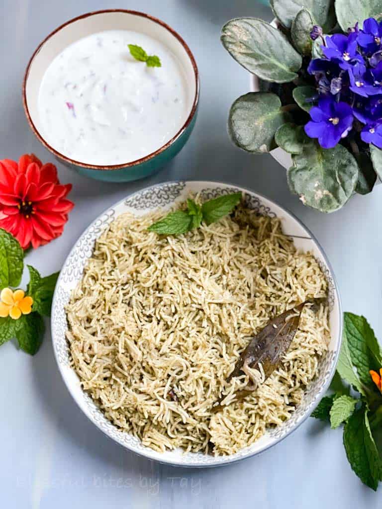 Mint pulao in a bowl with mint leaves as garnish and onion Raita on the side.