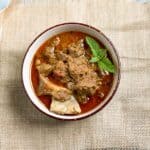 mutton curry in a bowl with mint leaf on top.