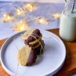 Stack of Almond cookies, half dipped in chocolate served with milk in a bottle.
