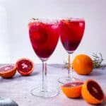 2 glasses of blood orange mocktail with cut up blood oranges on the side.
