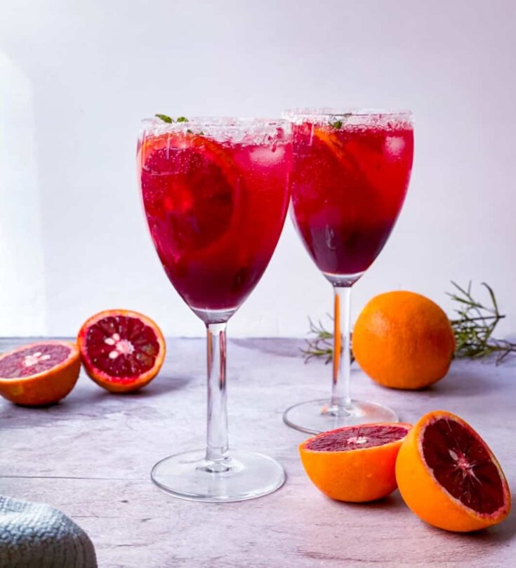 2 glasses of blood orange mocktail with cut up blood oranges on the side.