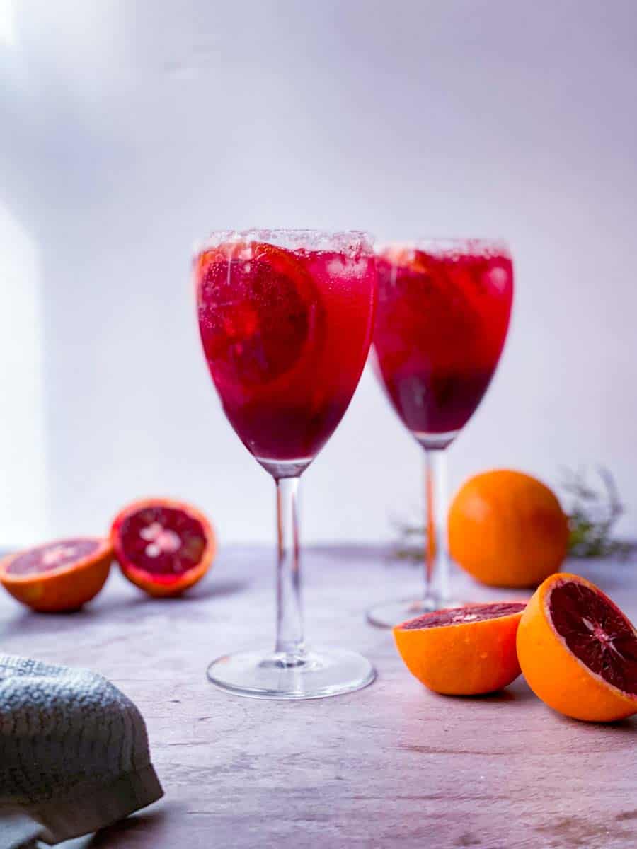 2 glasses of blood orange mocktail with blood oranges on the side.