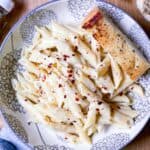 cream cheese pasta in a bowl with garlic bread on the side.