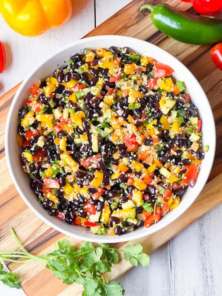Black bean and hemp salad in a white bowl on a wooden chopping board.