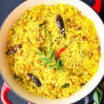 Mango pulihora in a dutch oven with curry leaves and chilies on top.