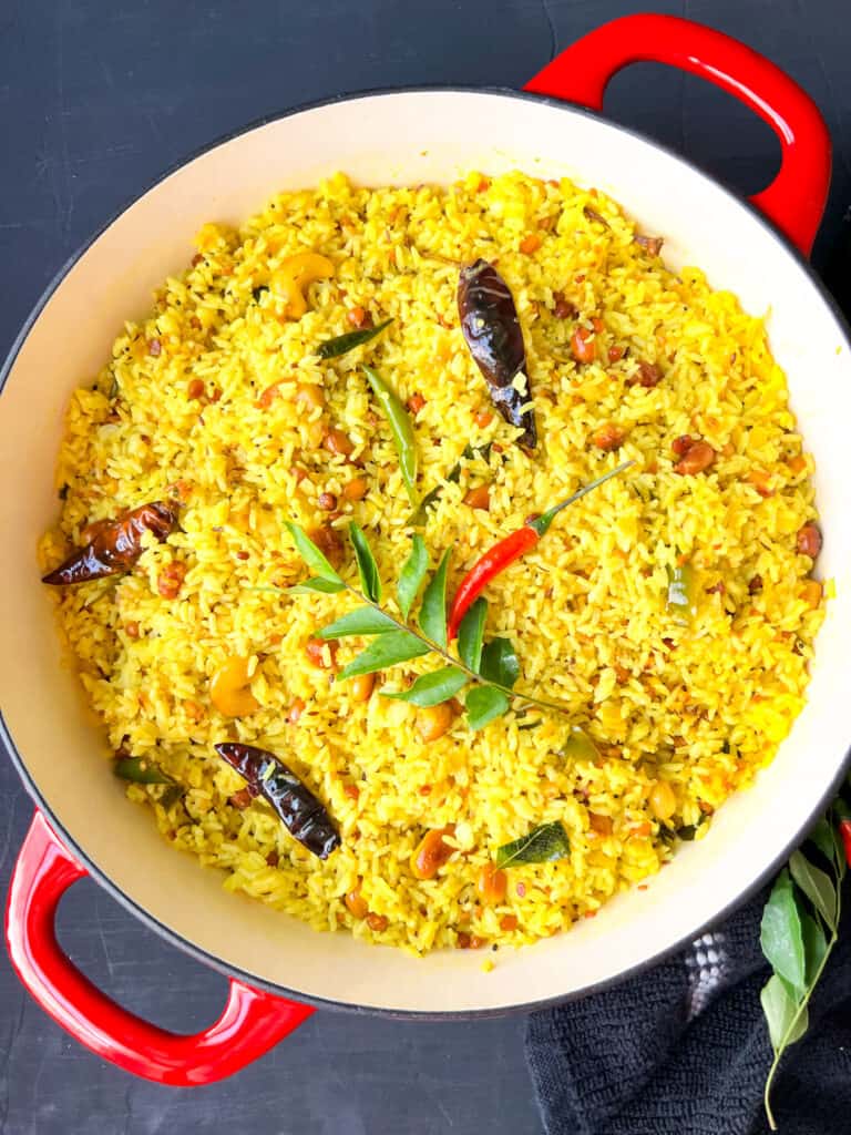 Mango pulihora in a dutch oven with curry leaves and chilies on top.